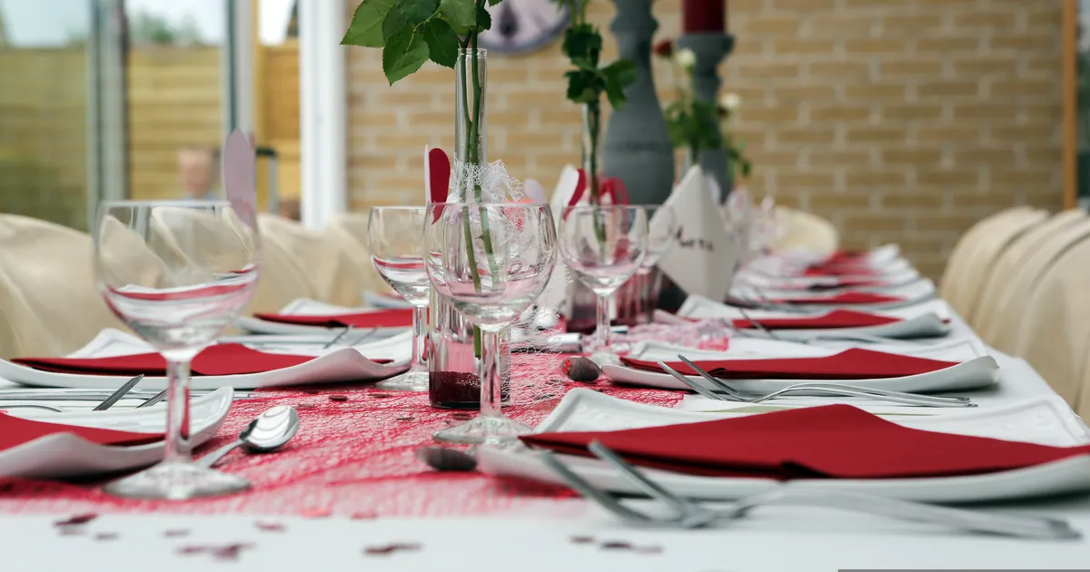 Tables de réception dressées avec serviettes rouges, verres et marque-places